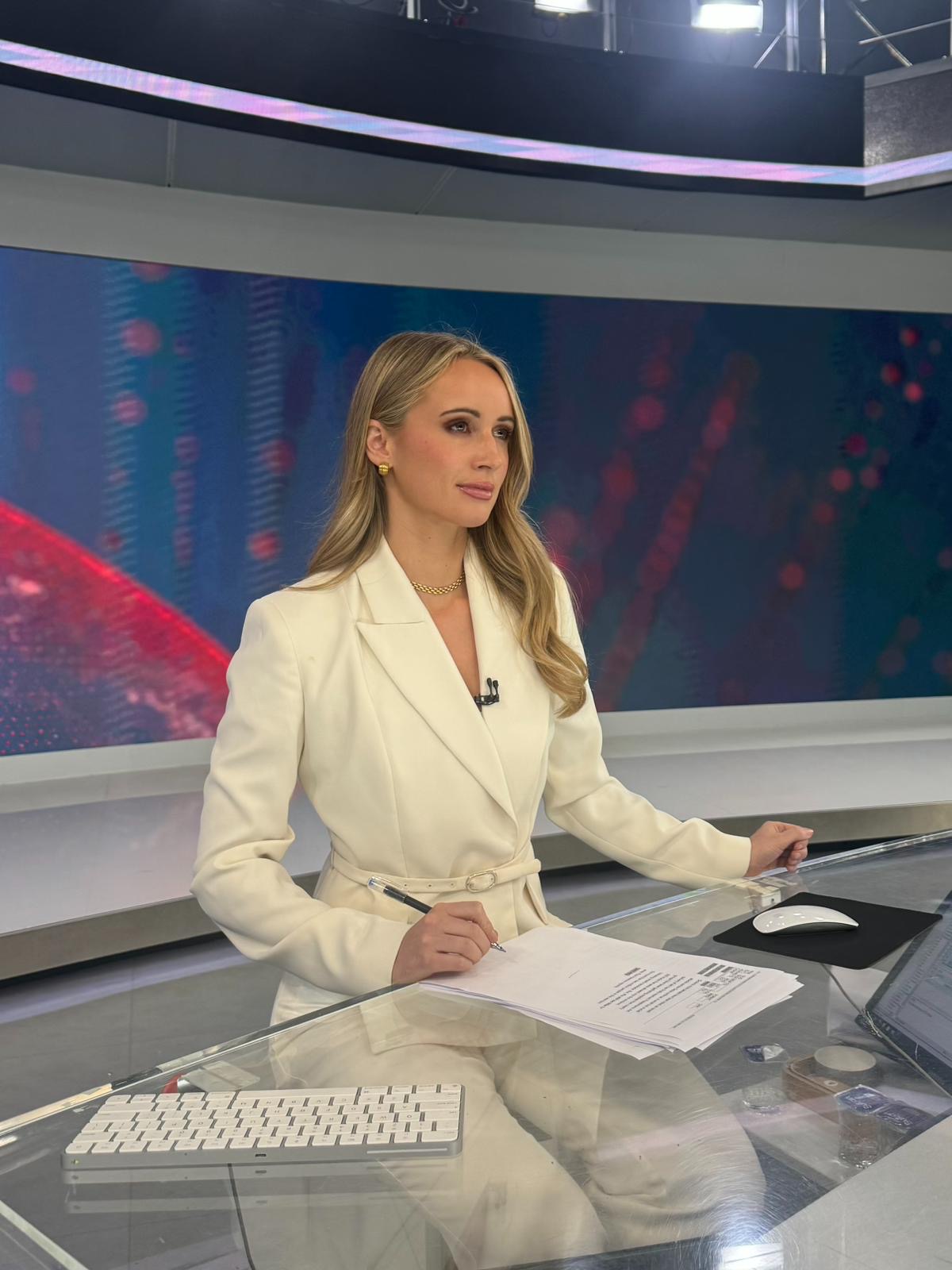 Charlotte Bates at the TRT World news desk in a white blazer, writing notes before going live