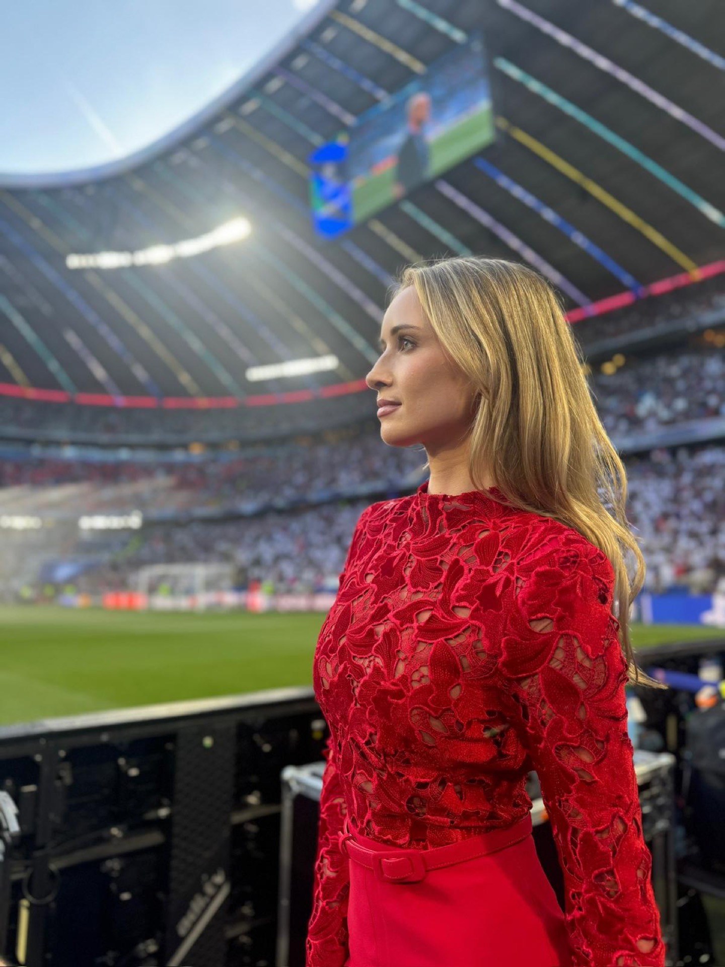 Charlotte Bates at a Champions League stadium in a red dress, looking over her shoulder