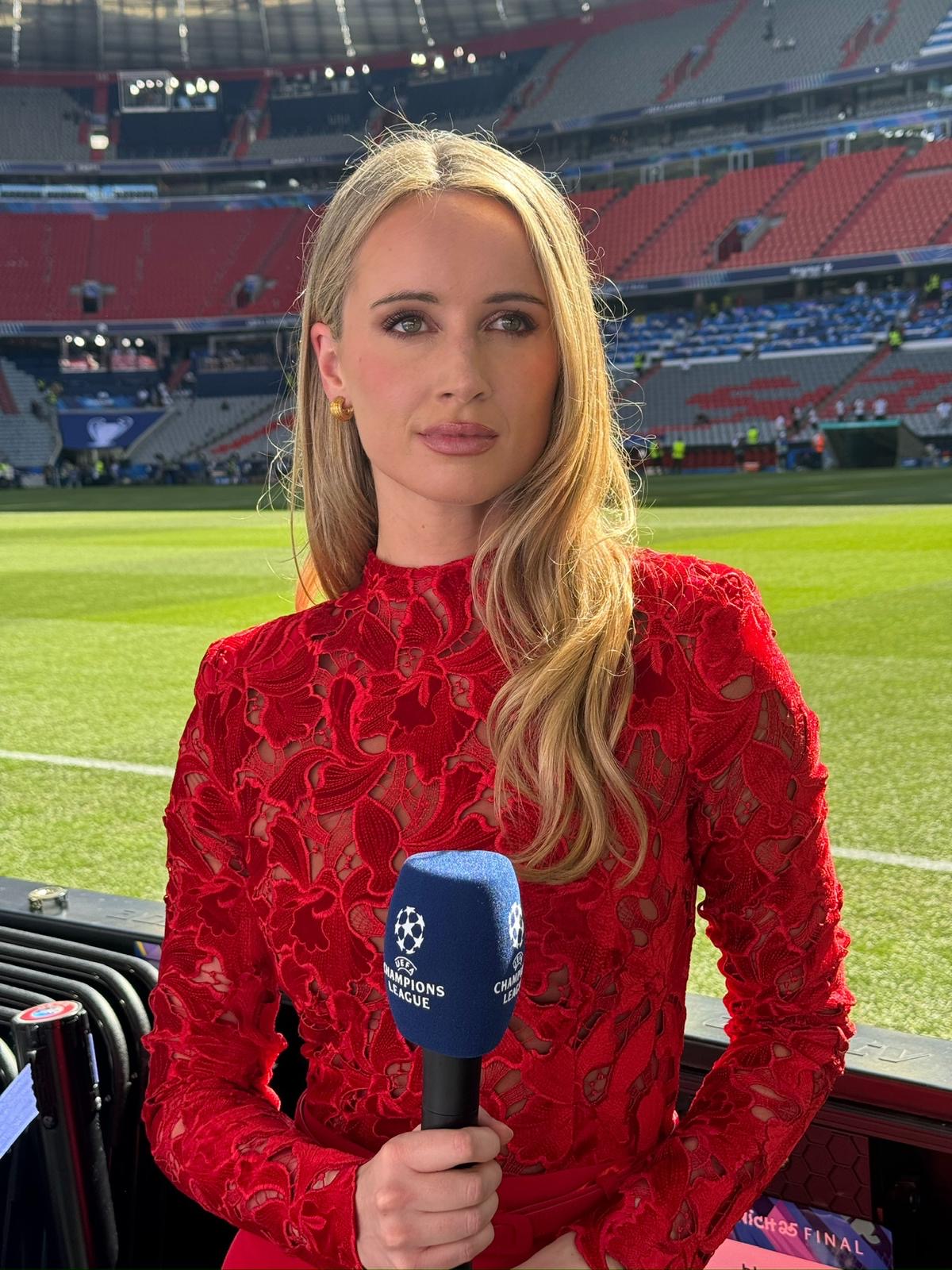 Charlotte Bates reporting live at the Champions League with a microphone, speaking directly to camera in a red dress