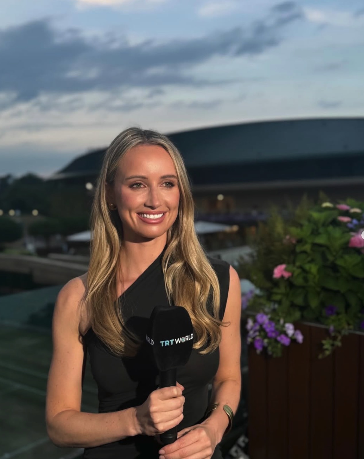 Charlotte Bates delivering a live rooftop report for TRT World with a city skyline behind her