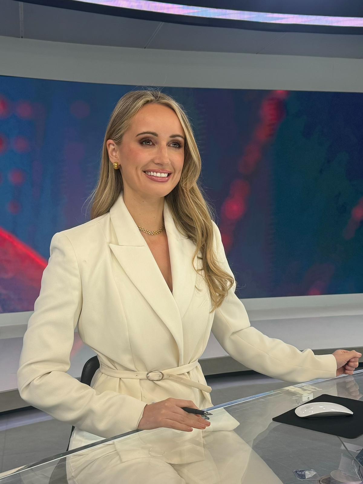 Charlotte Bates at the TRT World news desk in a white blazer, smiling warmly